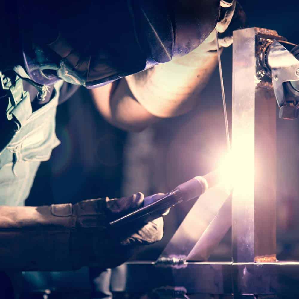 Masked welder operating a TIG welding torch with protective equipment, demonstrating precision heat management
