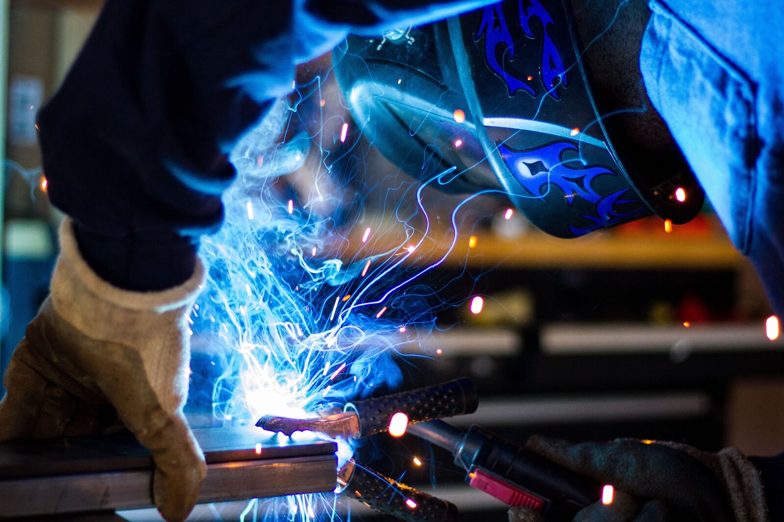 Industrial welder performing arc welding on structural steel with sparks and protective equipment